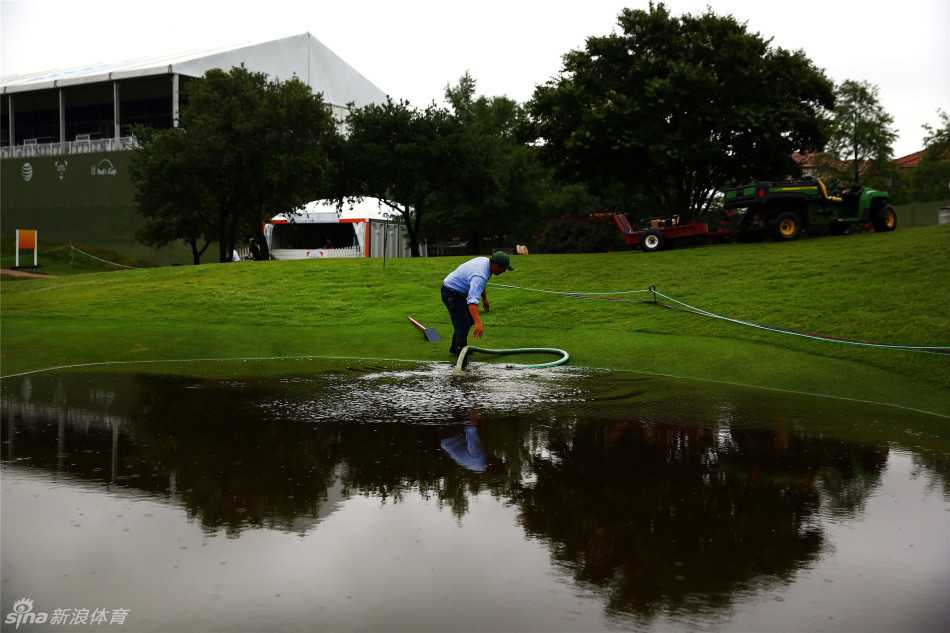 滂沱大雨袭赛场 四杆洞变三杆洞 尼尔森锦标赛上演水上高尔夫 一位球员在发球台沉思,他身后的球童举着伞,发球台前方是大片的水面,他的下一杆必须精准地越过这片水域